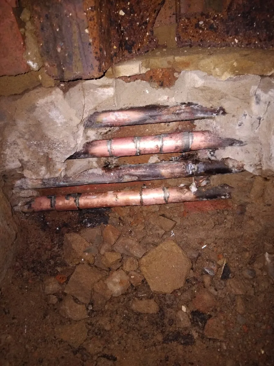 Emergency plumbing repair in progress with damaged copper pipework exposed inside a wall.