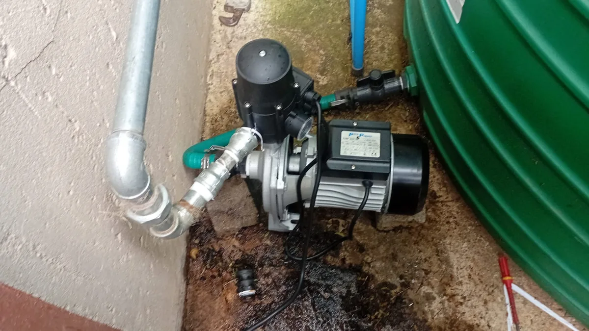 Greywater system plumbing with pump and connected pipework beside a storage tank.