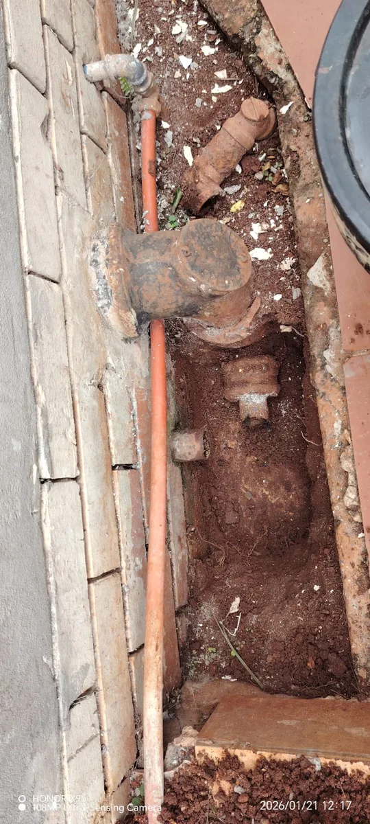 Replacement of old underground pipework opened in a trench beside a building.